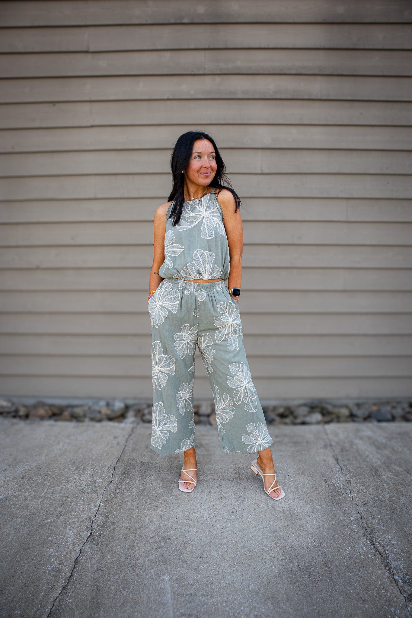 Woman wearing a green floral outfit standing against a gray wall.