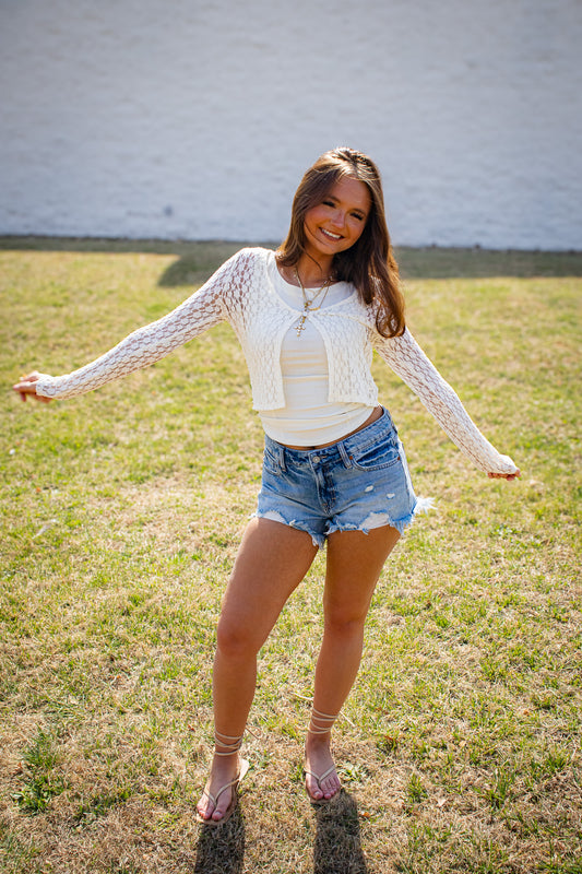 Woman in a white lace top and denim shorts standing in a grassy field.