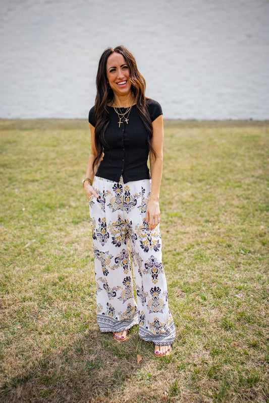 Woman wearing a black top and floral pants standing in a grassy field.