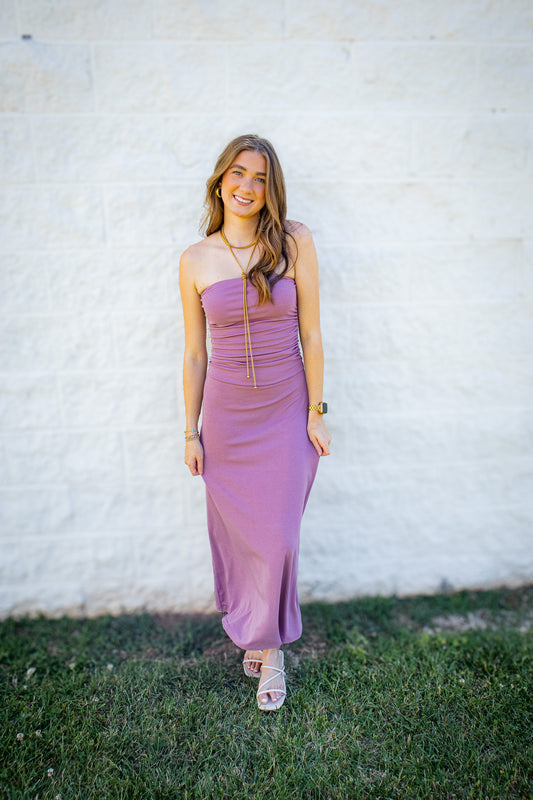 Women’s mauve strapless midi dress with ruched bodice styled with white heels and gold jewelry for a summer event outfit.