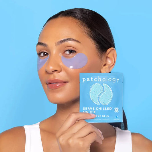 Woman with under-eye patches holding a box of patchology eye gels against a blue background