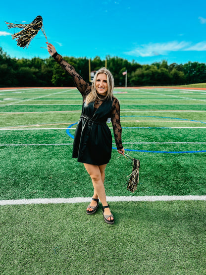 Woman in a black faux leather dress holding pom-poms on a football field