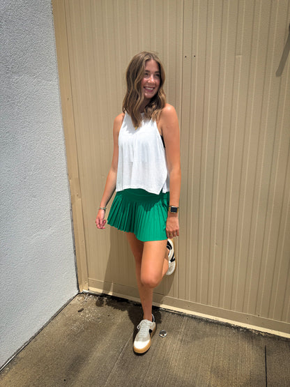 Woman in a white top and green skirt standing against a beige wall.