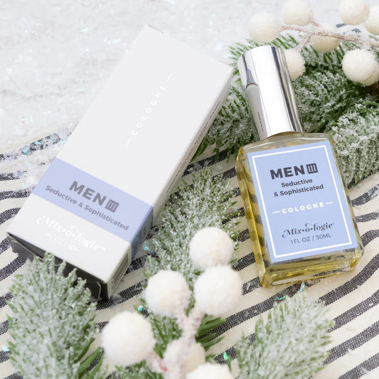 Men's cologne bottle and packaging on a decorative surface with greenery and white balls.