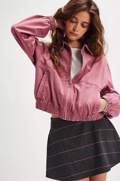 Woman wearing a denim dusty-rose zip-up jacket with elastic cuffs and hem, styled over a white knit top