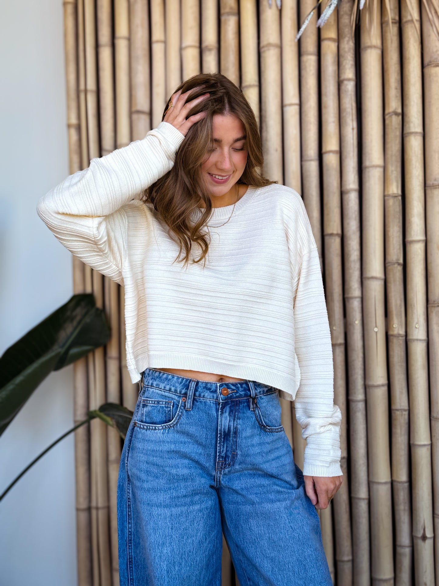 Cream textured knit sweater paired with relaxed blue denim, showcased on a model against natural bamboo for an elevated, effortless aesthetic