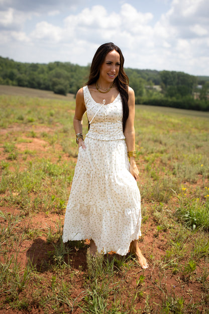 Woman in a white skirt set standing in a field with trees in the background