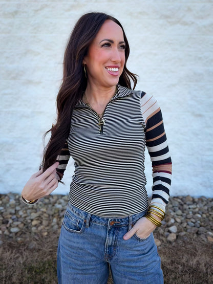 Woman wearing a striped long-sleeve top with multi-colored striped sleeves against a neutral background