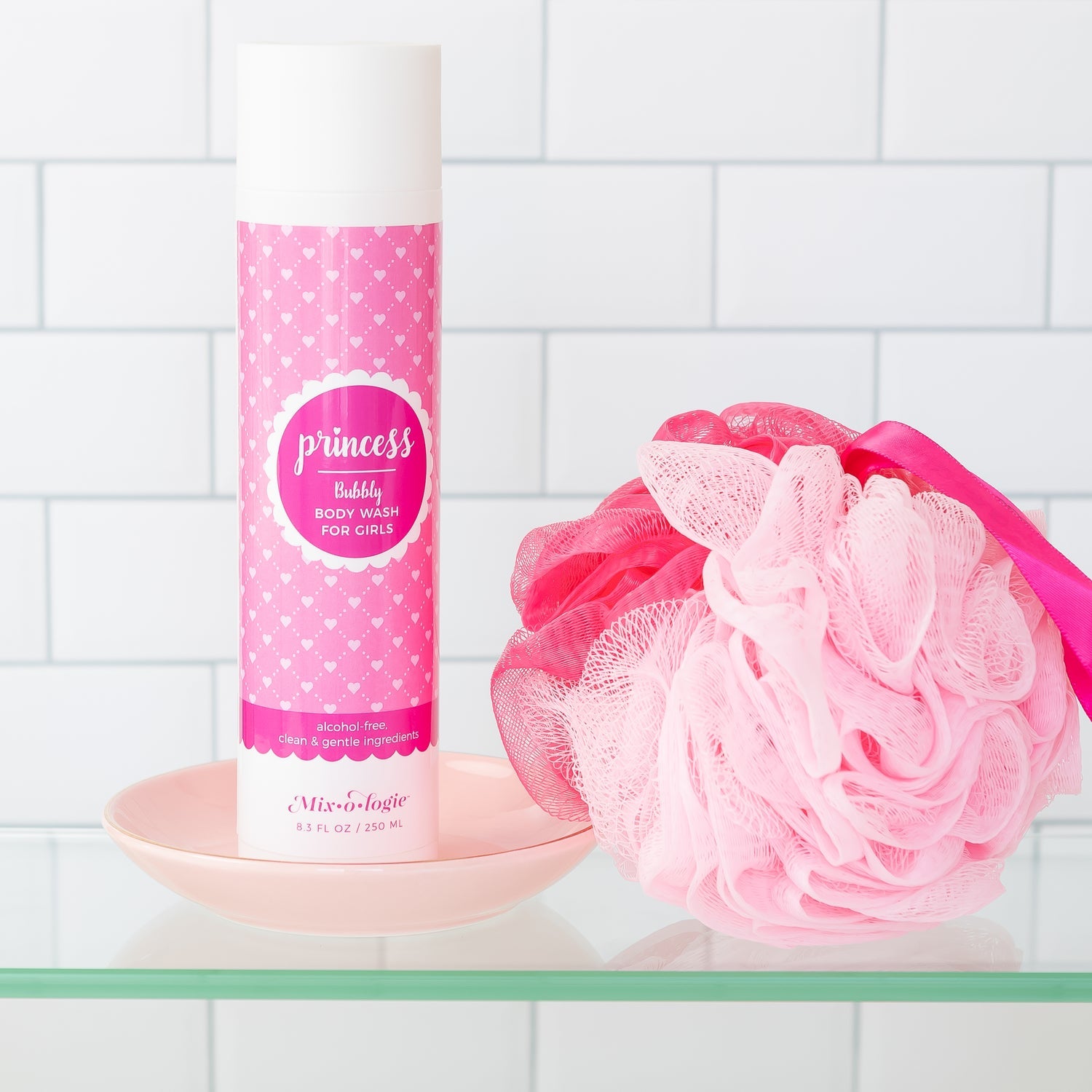 Pink 'princess' bubble bath bottle with a matching loofah on a tiled bathroom shelf.