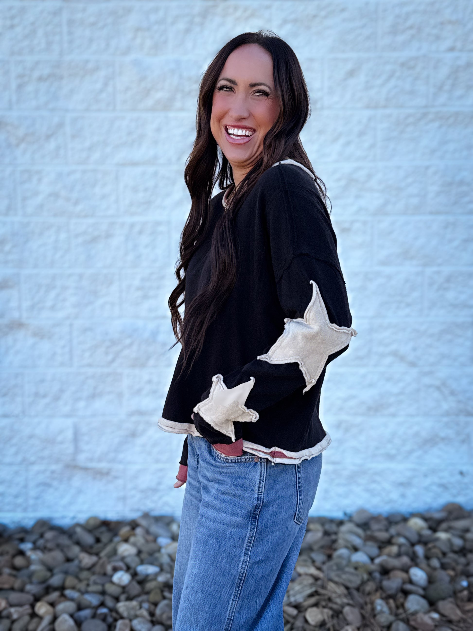 Woman wearing a black sweater with white star designs, standing against a textured white wall.
