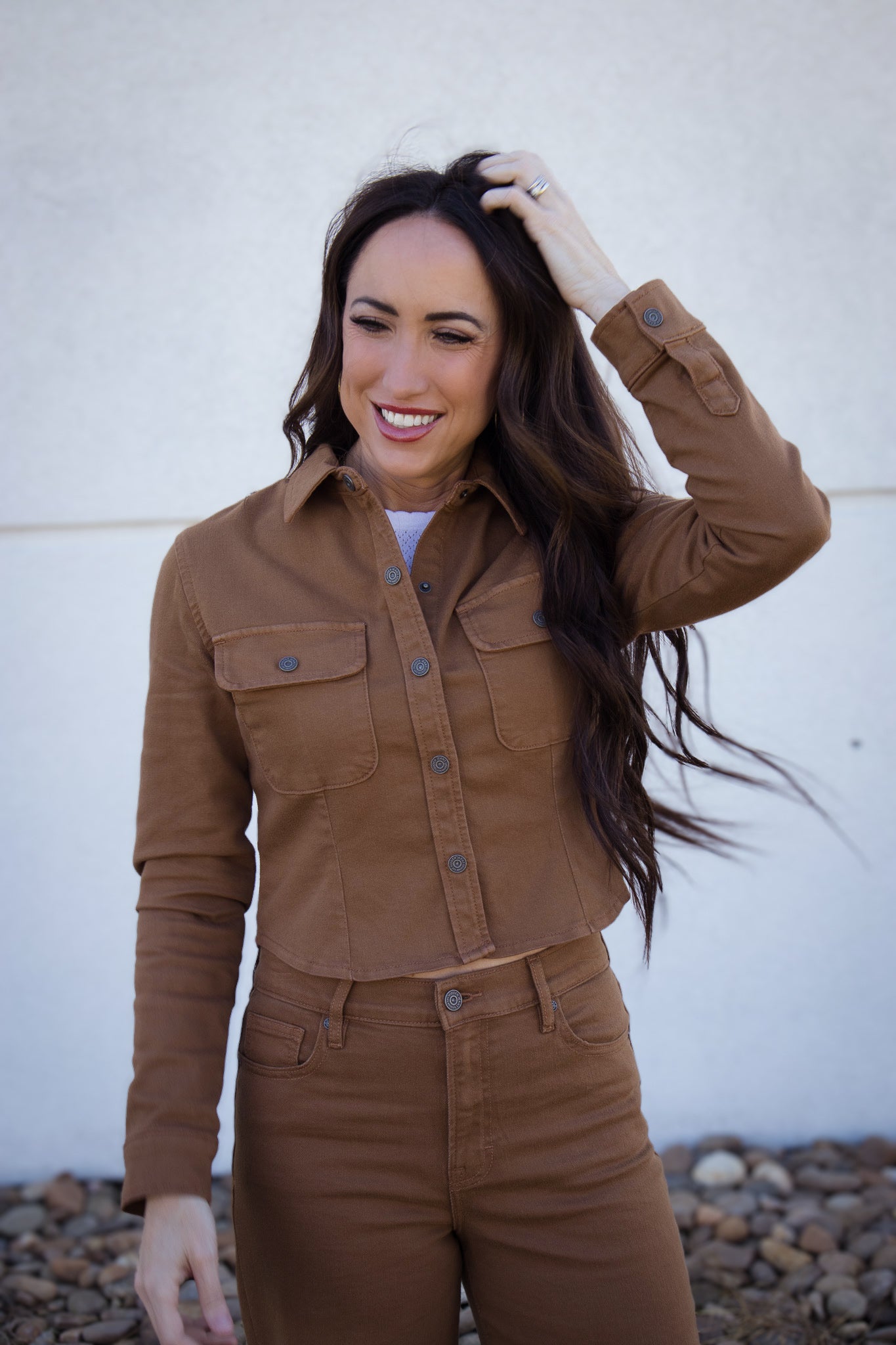 Woman wearing a brown jacket against a white wall.