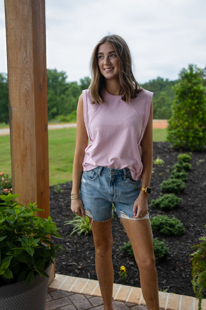 Woman wearing a pink sleeveless top and denim shorts standing outdoors.