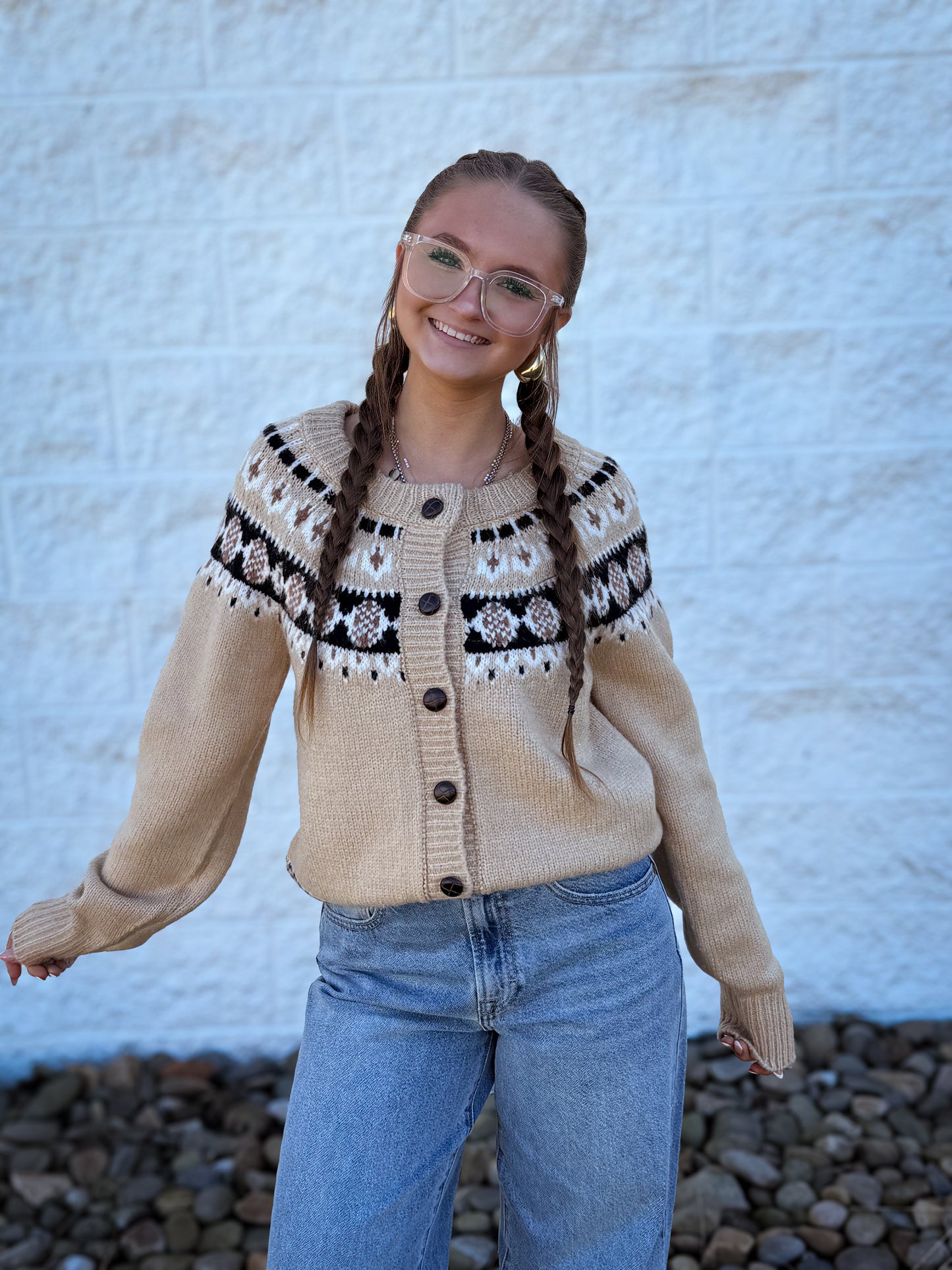 Person wearing a beige cardigan with black and white pattern, standing against a textured white wall.