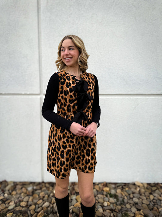Woman wearing a leopard print dress with a black top against a white wall.