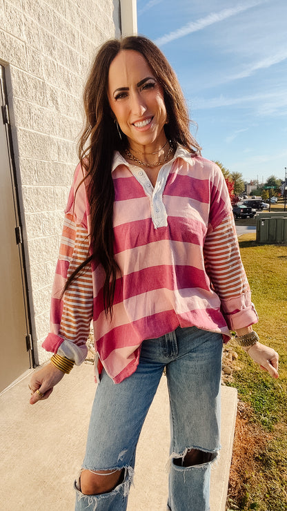 Woman wearing a pink, orange, and white striped shirt and blue, ripped jeans standing outdoors.