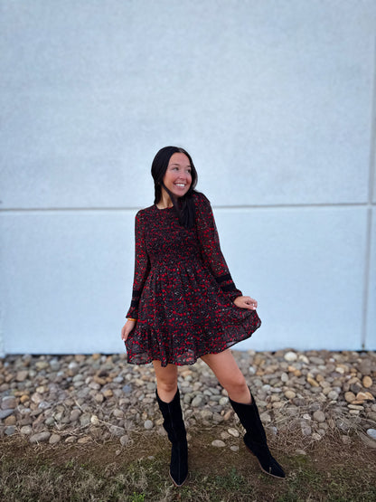 Woman wearing a floral dress and black boots standing against a light blue wall.