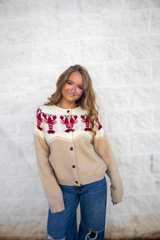 Woman wearing a beige and ivory sweater with red and black lobsters on it. 