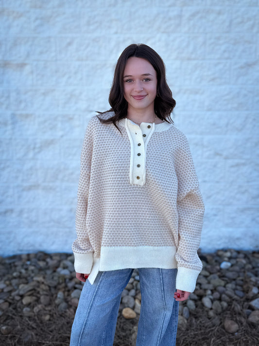 Person wearing a beige textured sweater with a white collar against a textured white wall.