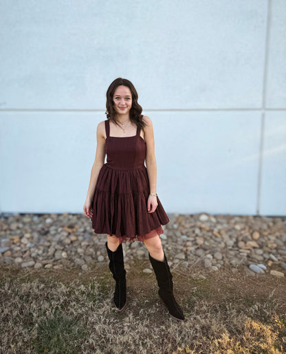 Woman wearing a burgundy dress and black knee-high boots standing against a white wall.