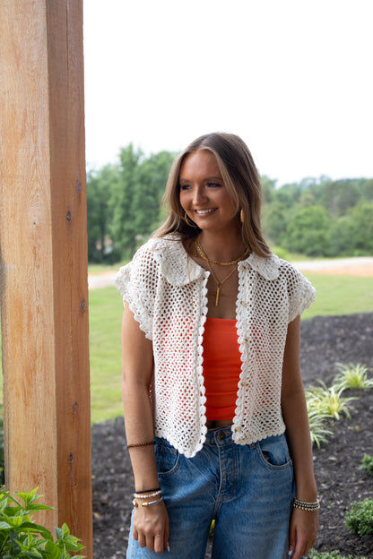 Woman wearing a white crochet top over an orange tank and jeans 