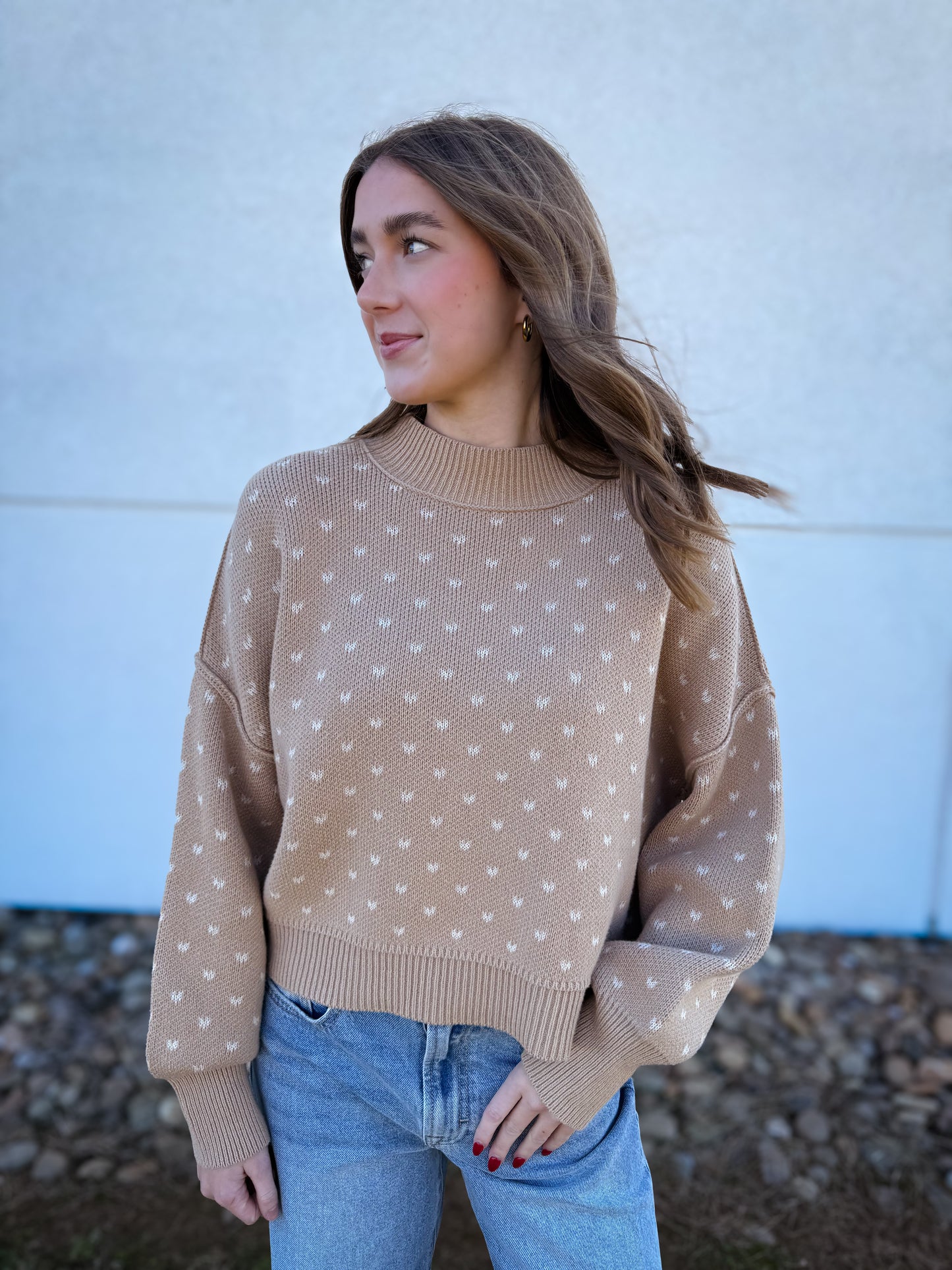 Woman wearing a beige mock neck sweater with white heart patterns and blue jeans