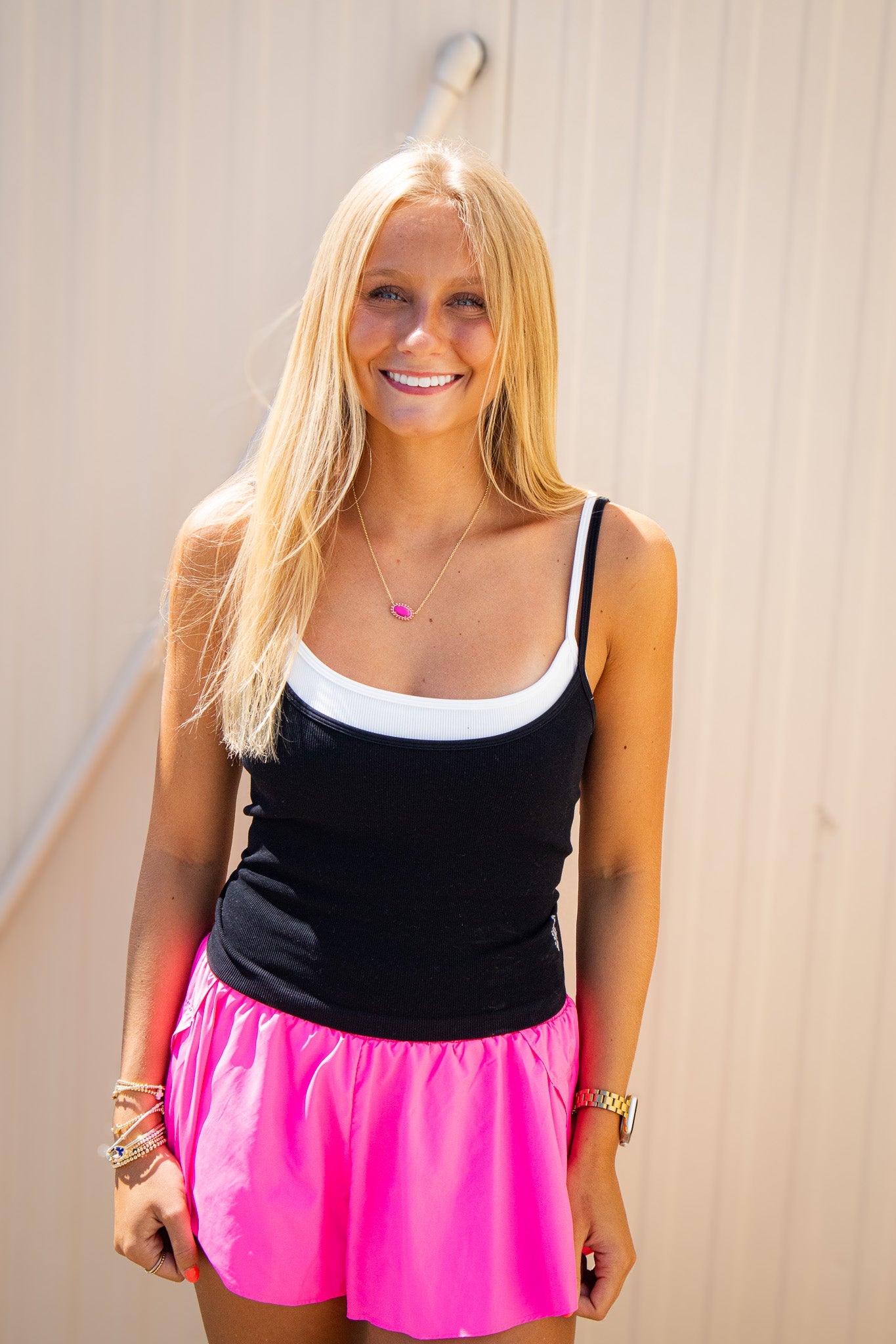 Black ribbed cami tank styled with a white layering tank, bright pink flowy shorts, and gold jewelry for a trendy summer boutique outfit.