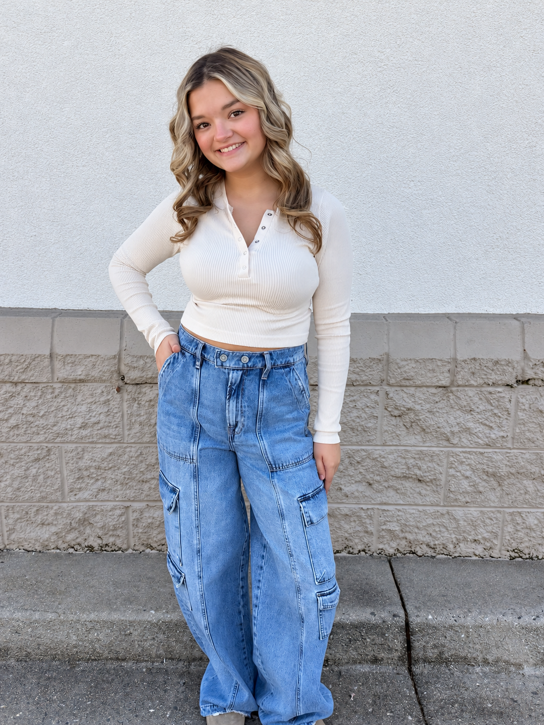 Model wearing the All Day Cropped Ribbed Long Sleeve Henley in Cream, featuring a fitted silhouette, soft ribbed texture, scoop neckline with functional buttons, and long sleeves, styled with light-wash wide-leg cargo jeans.