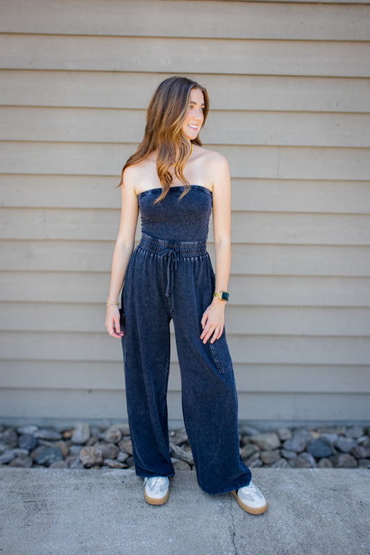 Women’s dark mineral wash strapless wide leg jumpsuit with smocked drawstring waist styled with sneakers.