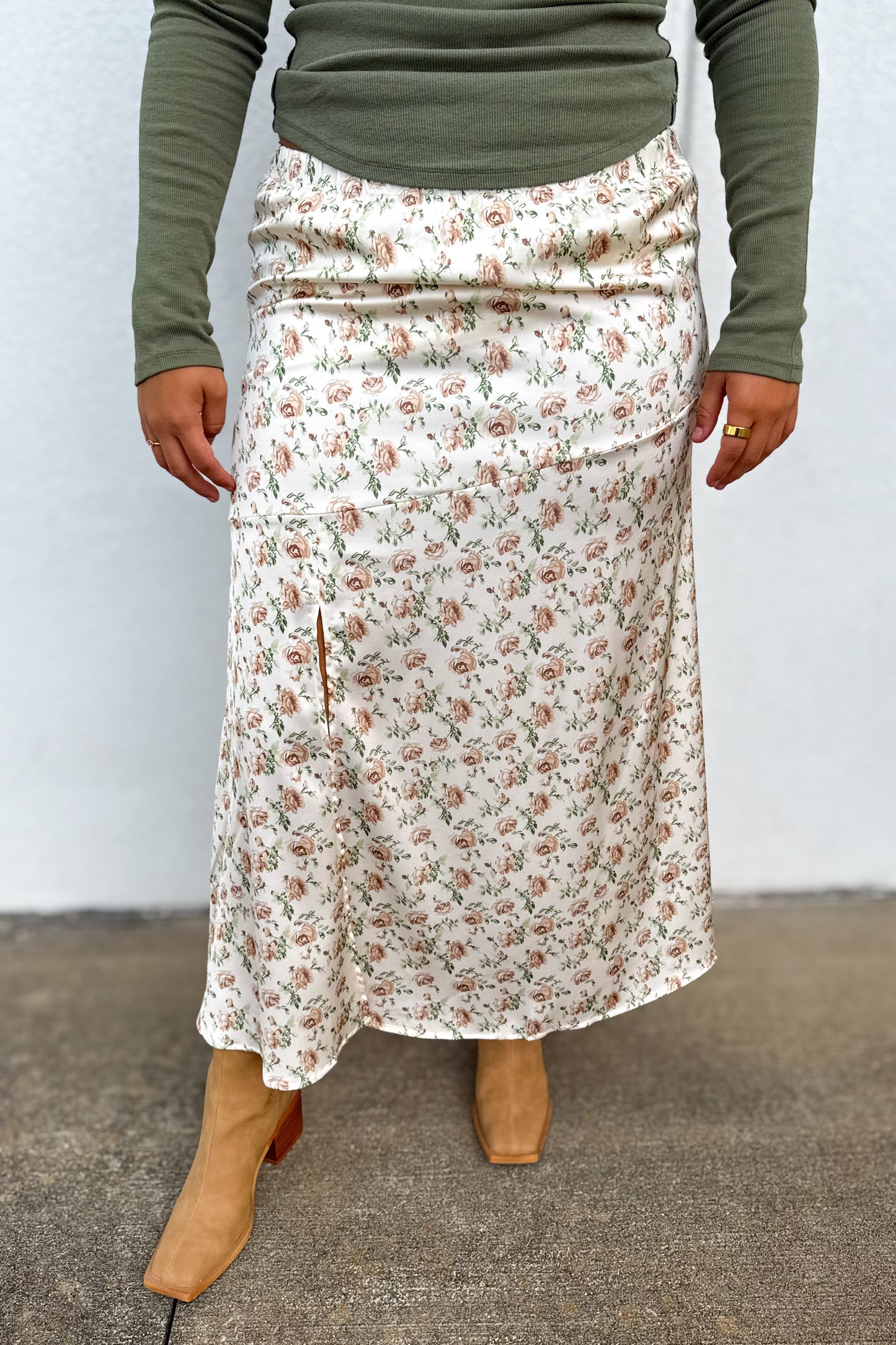 A person wearing a cream midi skirt with a small pink and green floral print, styled with an olive green long-sleeve top and tan boots.