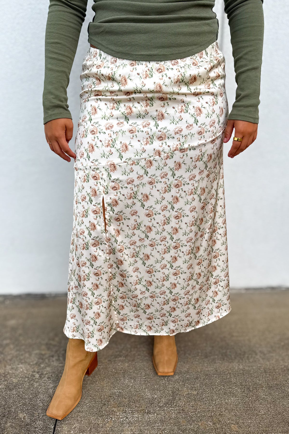 A person wearing a cream midi skirt with a small pink and green floral print, styled with an olive green long-sleeve top and tan boots.