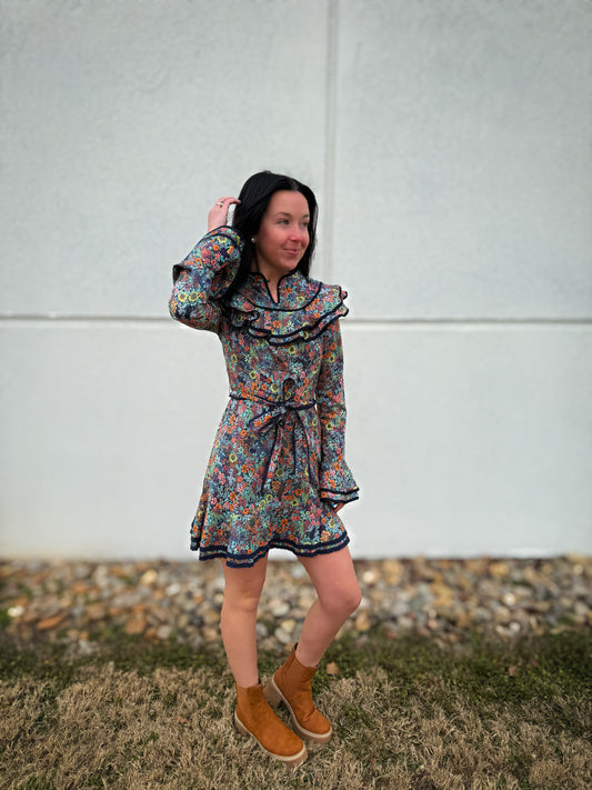 Woman wearing a floral dress and brown boots standing against a plain background