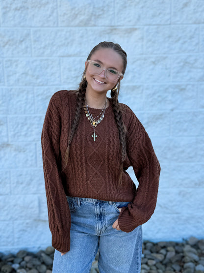 Chocolate brown cable knit sweater featuring an intricate textured knit pattern, classic crew neckline, ribbed cuffs and hem, and a relaxed fit for a cozy, timeless fall and winter look.