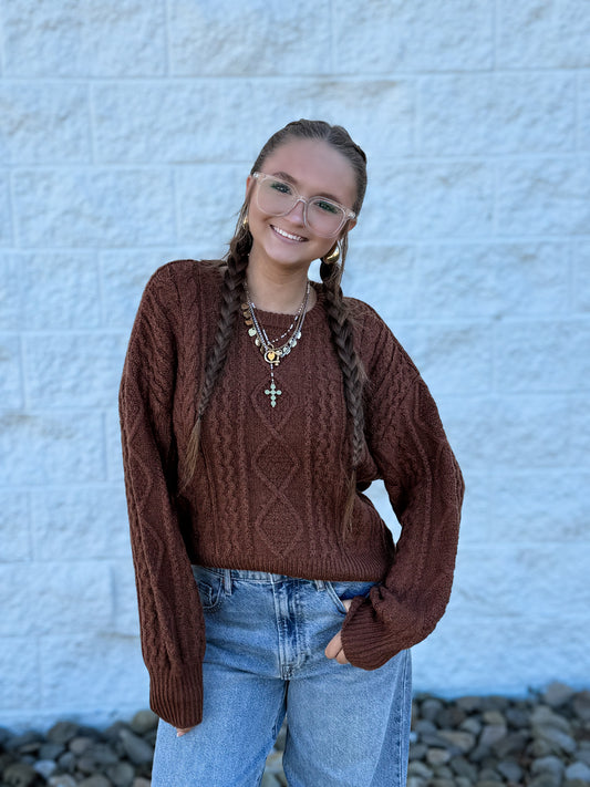 Chocolate brown cable knit sweater featuring an intricate textured knit pattern, classic crew neckline, ribbed cuffs and hem, and a relaxed fit for a cozy, timeless fall and winter look.