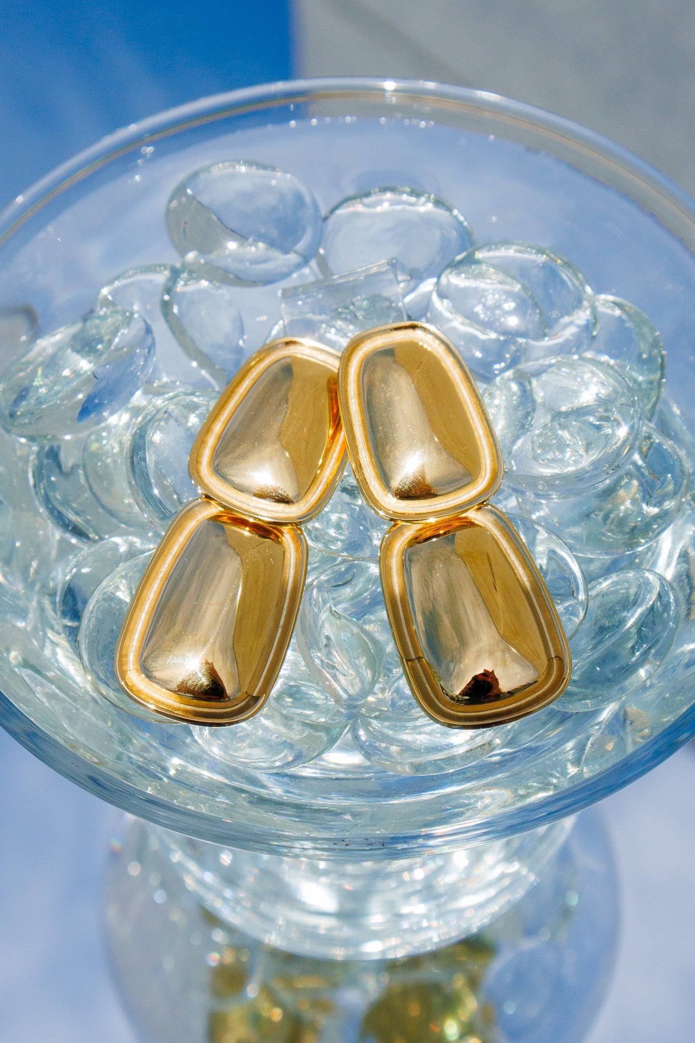 Gold earrings on a glass of water with ice cubes