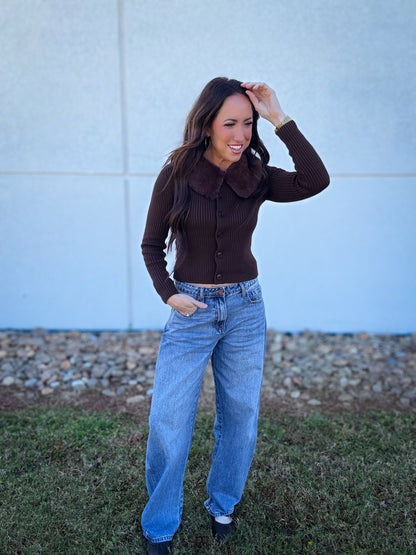 Woman wearing a brown sweater and blue  Baggy barrel jeans standing outdoors.