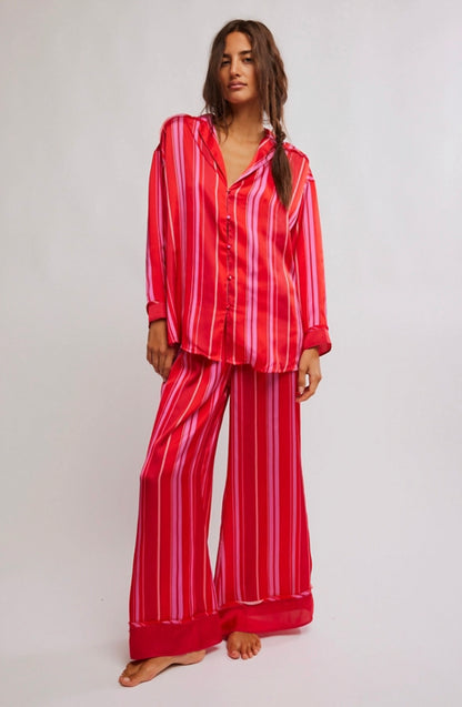 Woman wearing a silk, red and pink striped pajama set against a plain background