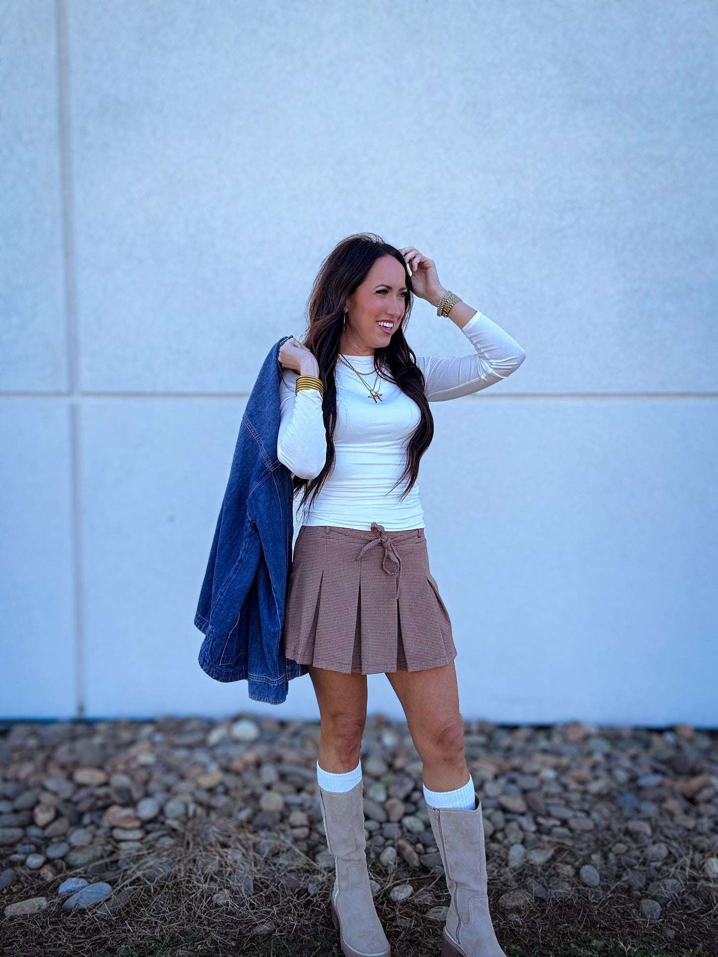 Women wearing a plaid pleated skort with a white long sleeve top and a denim shacket. Paired with tall boots and boot socks 