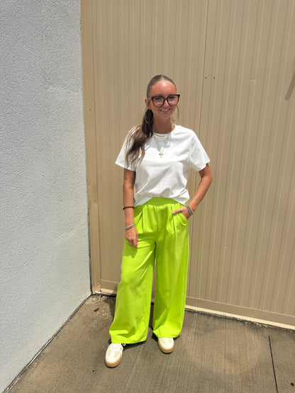 Person wearing a white shirt and bright green pants standing on a concrete surface.