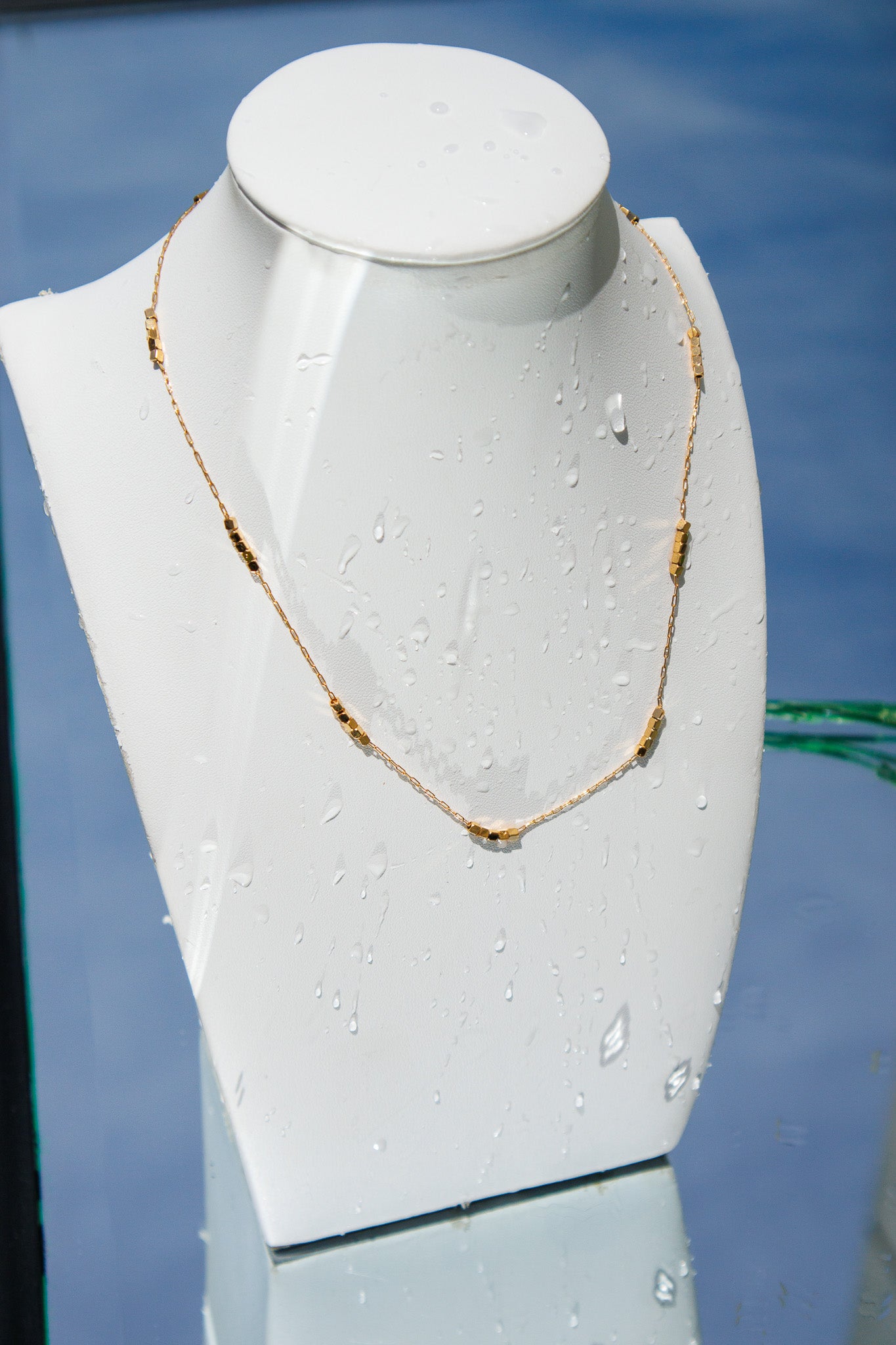 Gold necklace on a white mannequin bust against a blue background