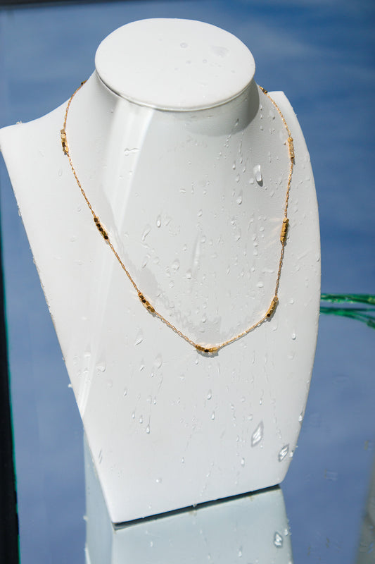Gold necklace on a white mannequin bust against a blue background