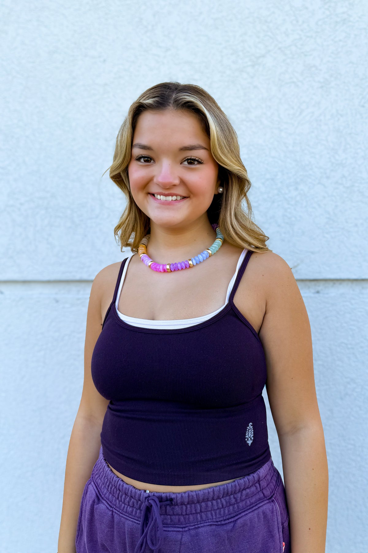 Model wearing the Free People All Clear Coastline Cami in Mars/Cool Lilac, featuring a fitted ribbed design, scoop neckline, thin straps, and contrasting cream trim, styled with purple drawstring shorts.