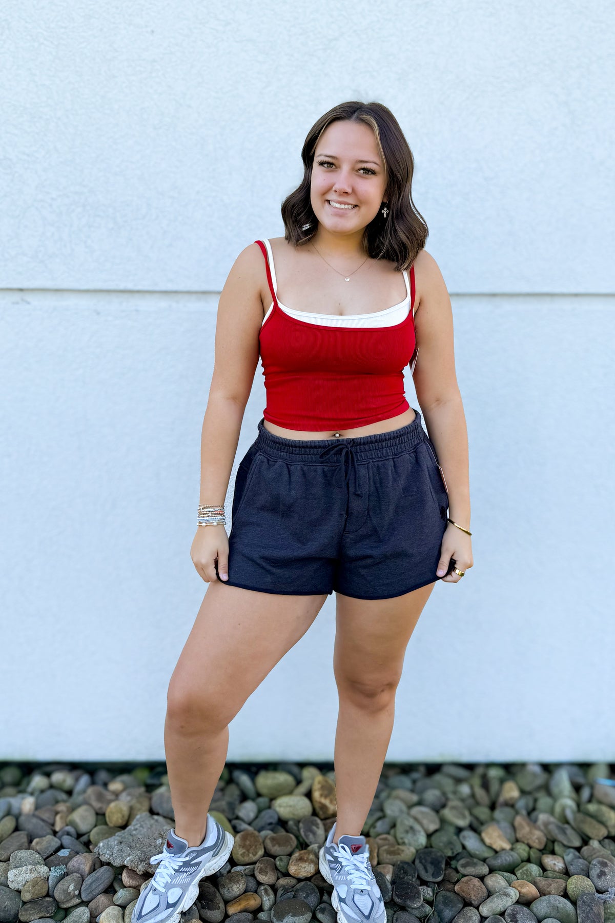 Model wearing the Free People All Clear Coastline Cami in Red/Cream, featuring a fitted ribbed design, scoop neckline, thin straps, and contrasting cream trim, styled with black drawstring shorts.