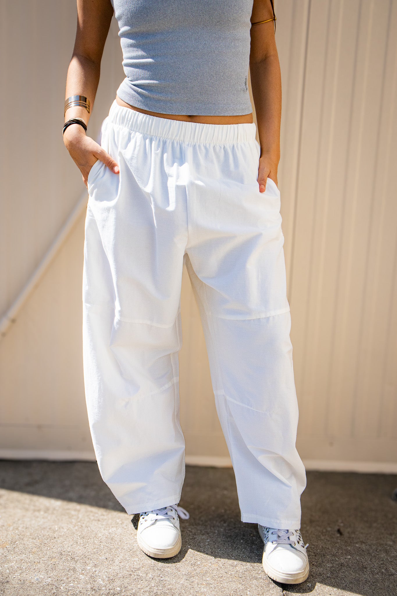 Person wearing a grey top and white Free People barrel pants standing against a neutral background
