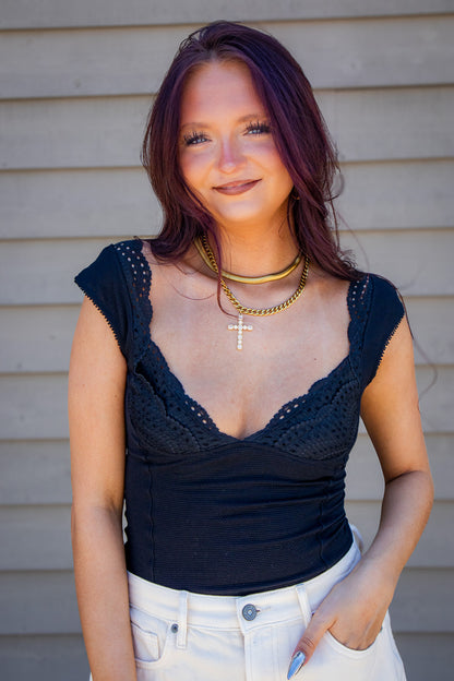 Black crochet lace cap sleeve bodysuit styled with white denim and layered gold jewelry for a trendy boutique outfit, perfect for summer nights, concerts, date night, and going out looks.
