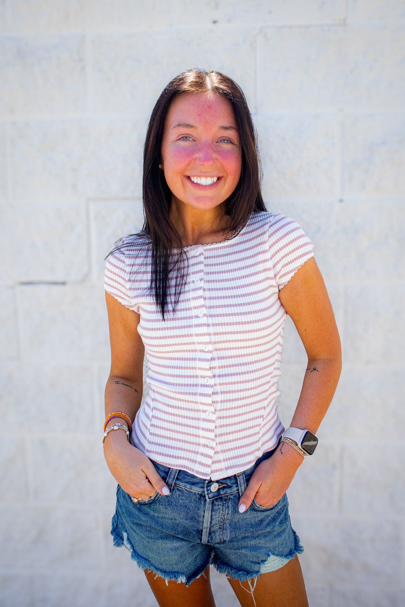 Woman wearing a striped shirt and denim shorts against a light background