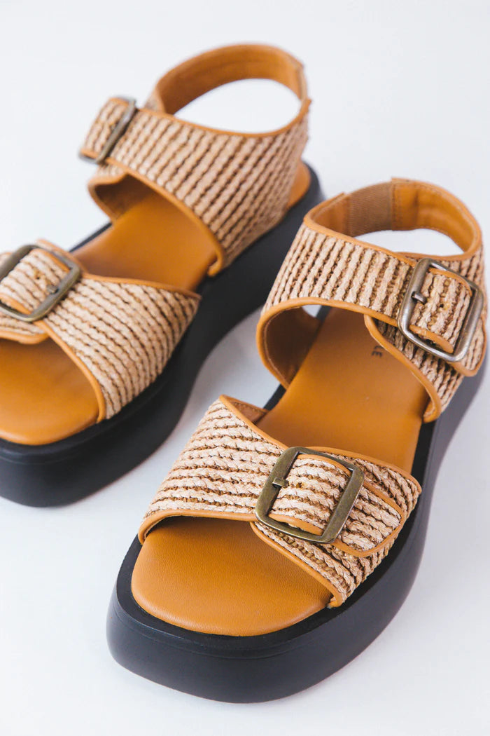 Pair of woven sandals with brown straps on a white background