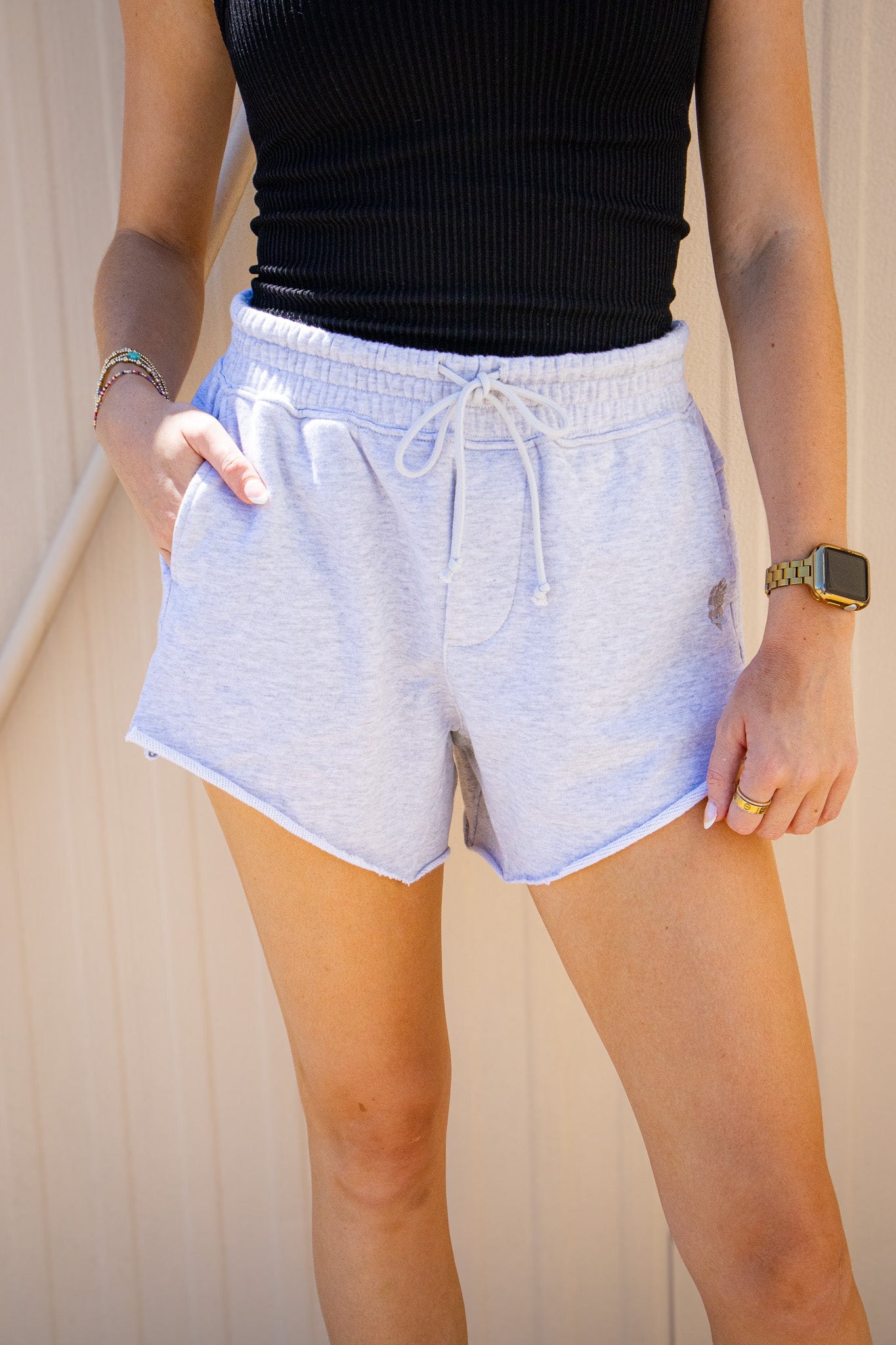 Light gray Free People drawstring lounge shorts with elastic waistband, side pockets, and raw hem styled with a black ribbed tank for a casual summer outfit.