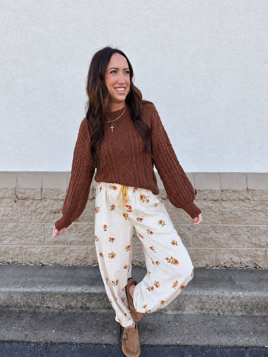 Model wearing Free People On Repeat Drawstring Pants in Ivory Floral, featuring delicate floral prints, subtle vertical stripes, a relaxed wide-leg fit, elastic drawstring waistband, and cuffed ankles, styled with a brown cable-knit sweater and tan loafers.