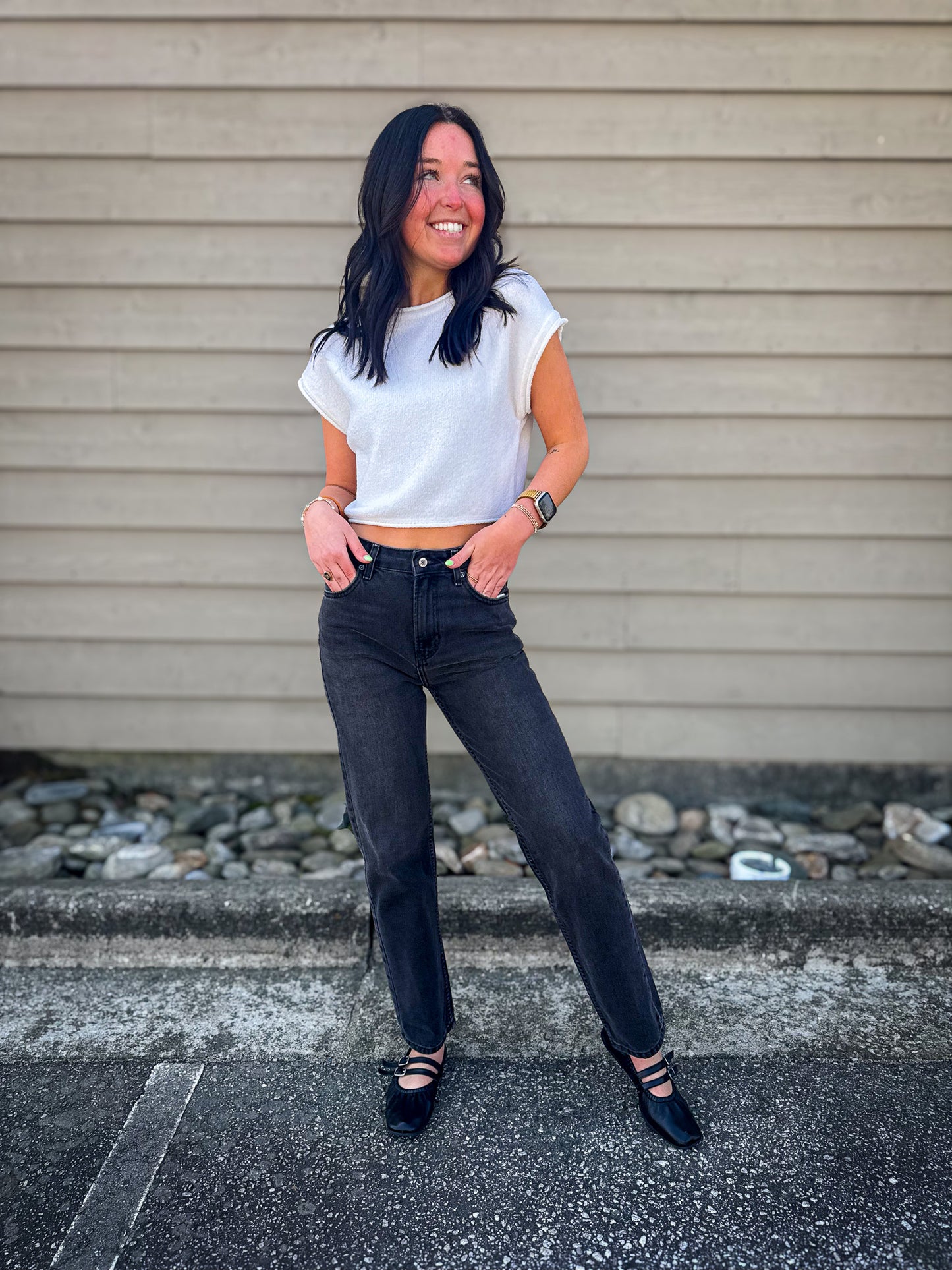 Woman wearing a white crop top and black Free People straight leg jeans standing against a beige wall.