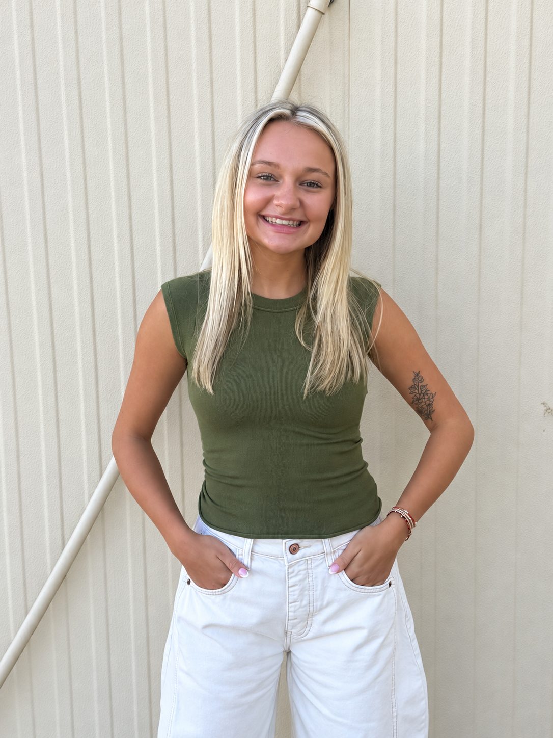 Model wearing the Free People So Soft Seamless Modal Baby Tee in Ferngully Olive, featuring a fitted ribbed design, crew neckline, cap sleeves, and waist-length silhouette, styled with white denim jeans for an effortless everyday look.